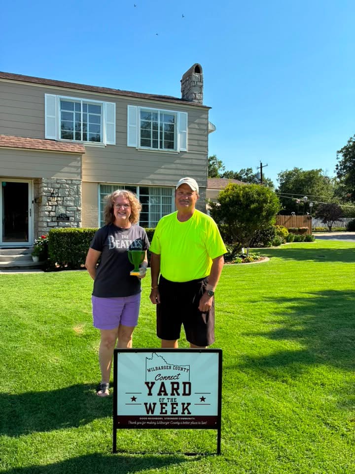 Greg and Emily Stone standing in front of their home on Paradise Street with the Yard of the Week sign